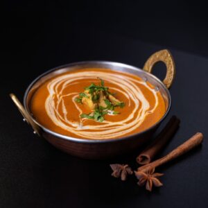 Vajas Csirke: A Fusion Grill egyik legkedveltebb fogása hagyományos indiai bronz tálban tálalva, fahéjjal és csillagánizzsal díszítve.