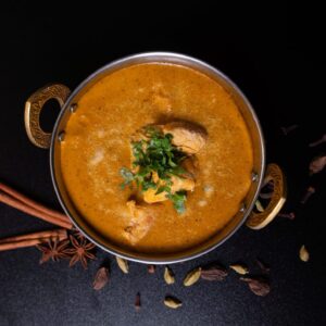 Kókuszos curry, szaftos csirkedarabokkal egy indiai stílusú tálkában, különböző fűszerekkel körbedíszítve.