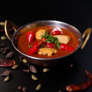 Chilivel és paprikával díszített Jalfrezi Csirke, klasszikus indiai tálban tálalva.