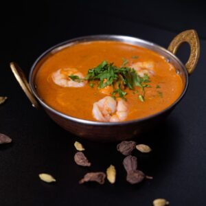 Garnélarákos csirkés curry, egy indiai stílusú bronz tálban, karadmomokkal díszítve