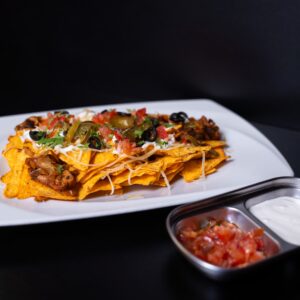 Egy tányérnyi nachos csirkedarabokkal mellette egy tálka salsa és tejfölös szósz