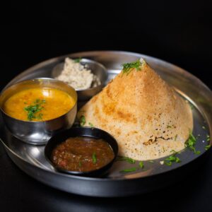 Egy fém tálcán kistálkákba elosztva, csatni, dhal, tejszínes mártogatós és egy dosa.