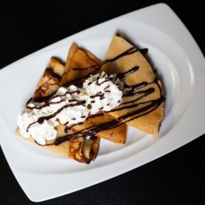 Három mogyorókrémmel töltött palacsinta, tejszínhabbal és csokiszósszal tálalva