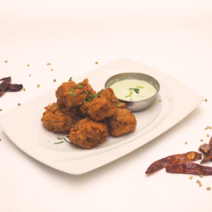 Kisütött zöldségfalatkák egy fehér tányéron, joghurtos szósszal tálalva, és szárított chilivel díszítve.